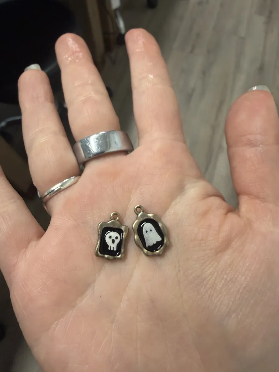 The finished ghost and skull charms in a palm, for scale
